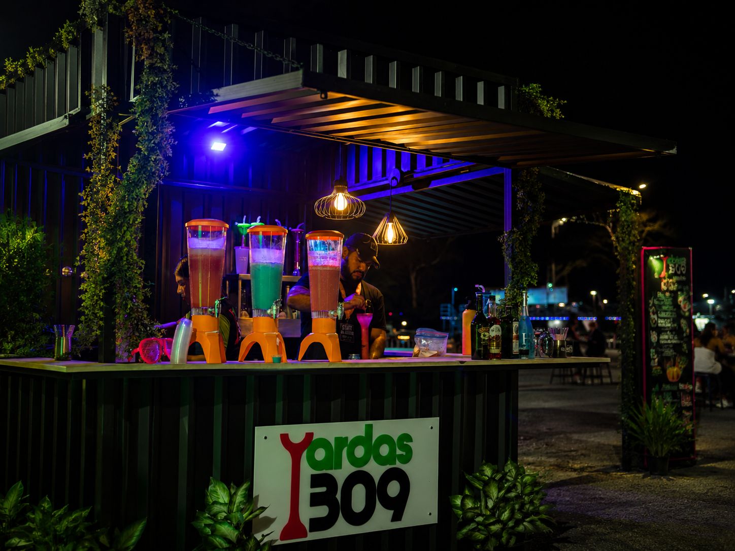 Barra de bar al aire libre de noche con licuadoras de cócteles de colores iluminadas
